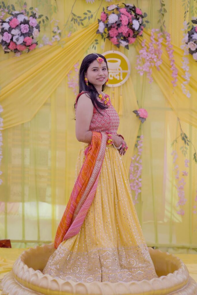 Woman posing in vibrant Indian traditional attire at a festive event decorated with flowers.